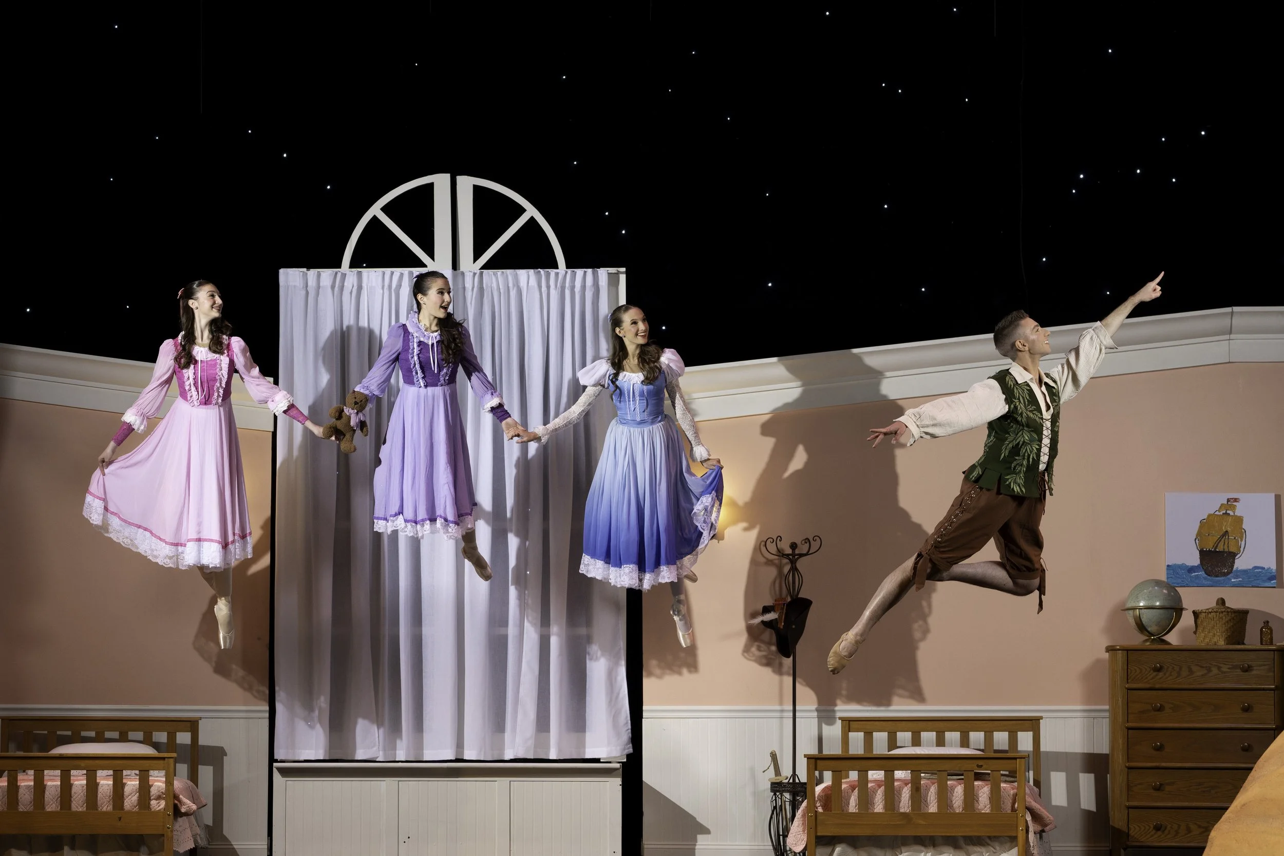 Five ballet dancers, four women in pastel dresses and one man in historical costume, performing on a stage with a bedroom set and a starry night backdrop.