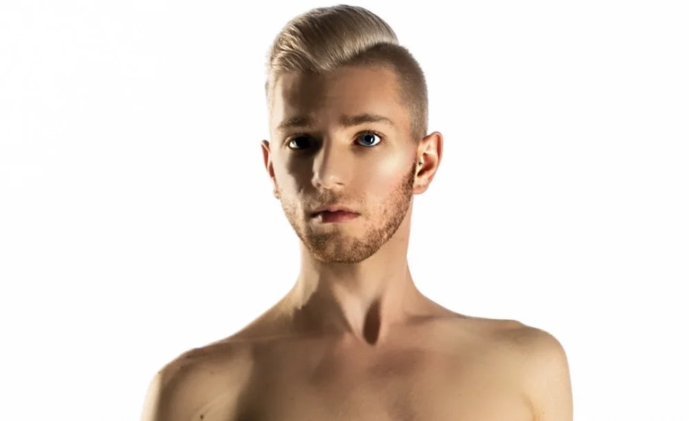 A shirtless young man with blonde hair and blue eyes looking at the camera against a white background.