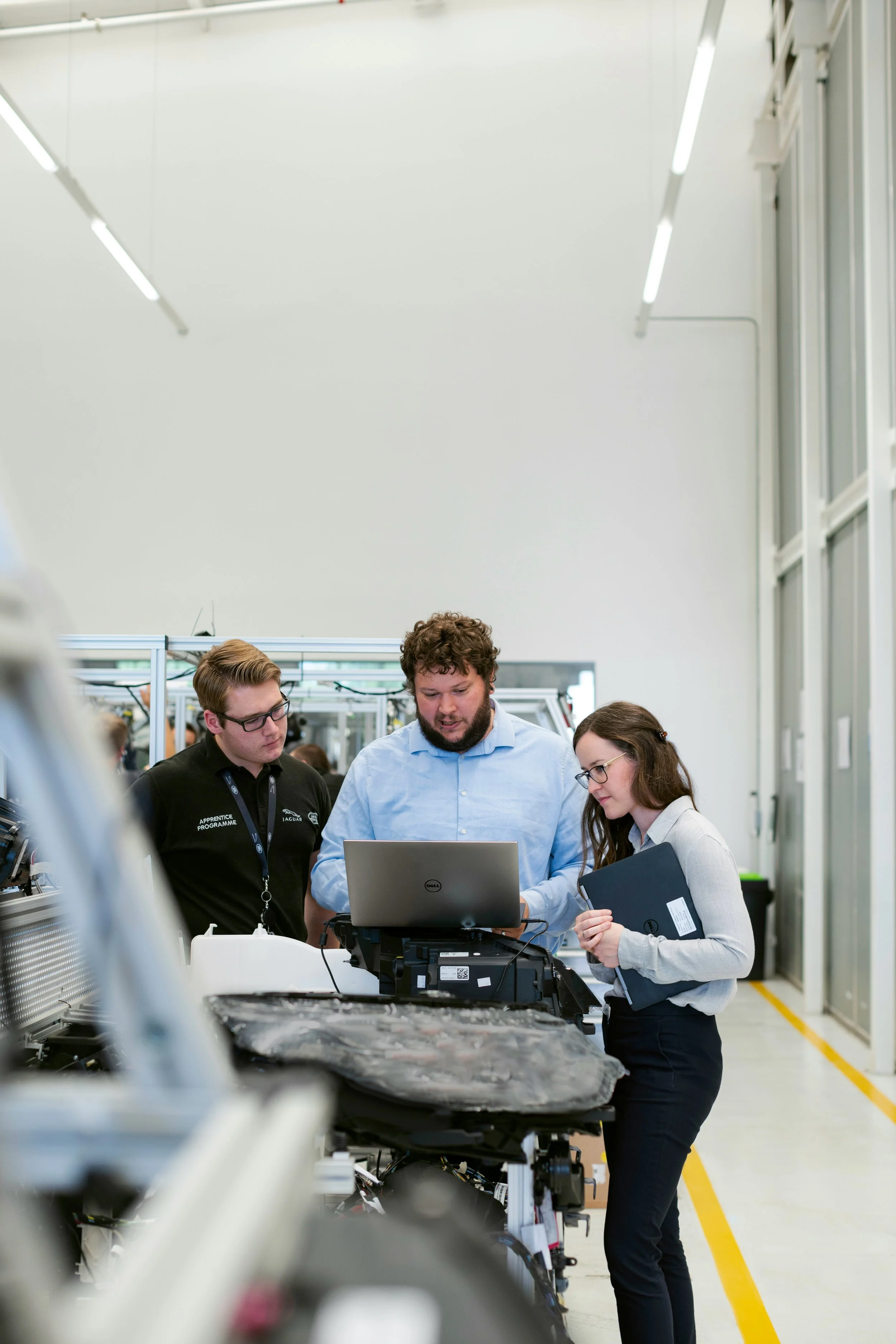 Three people working together in a laboratory or industrial setting, with equipment and machinery around them.