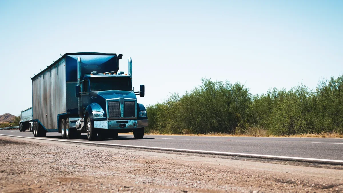 Tractor pulling a covered trailer on a two-lane highway under a clear sky