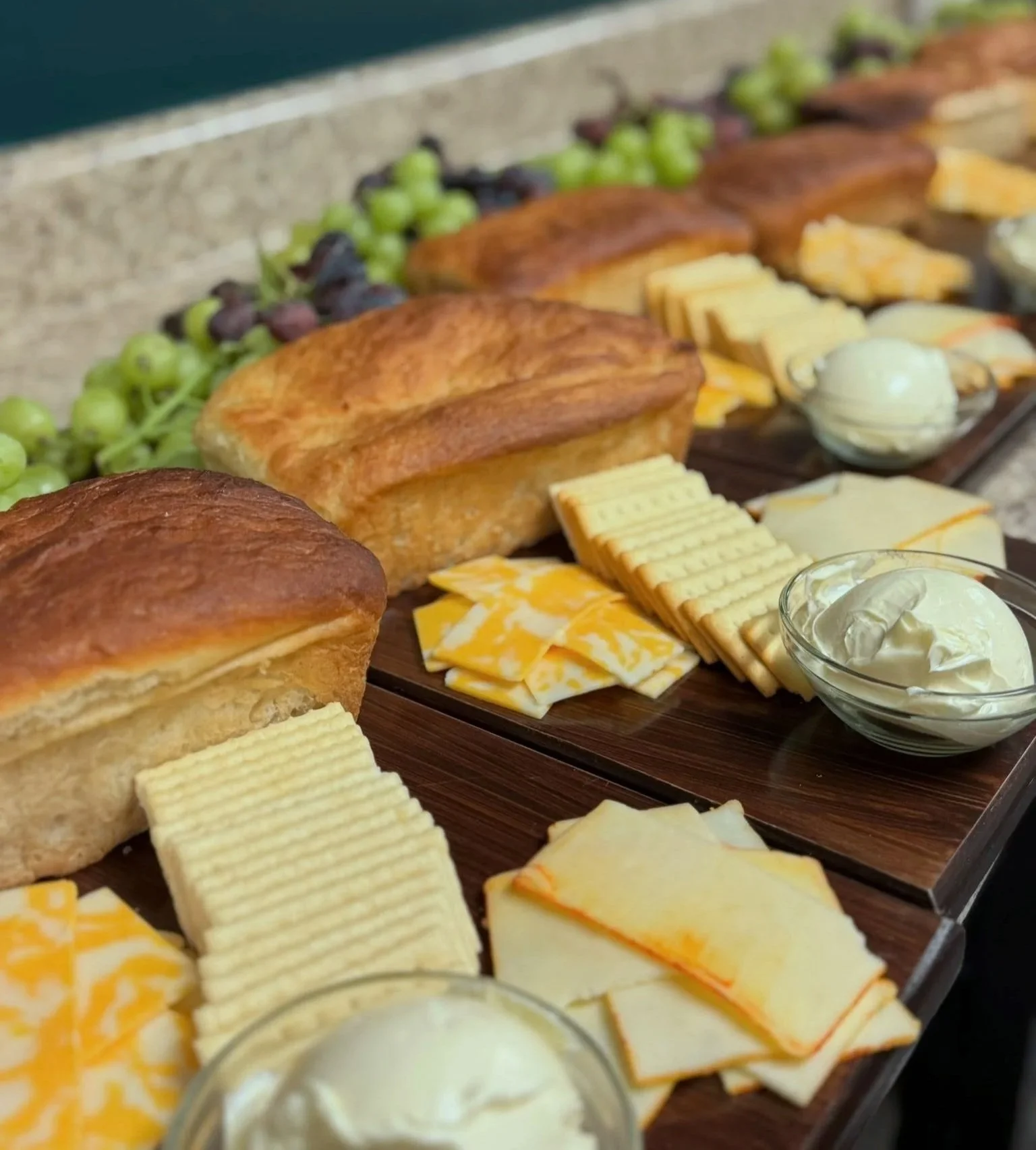A charcuterie board with various cheeses, bread, grapes, and small bowls of cream cheese.