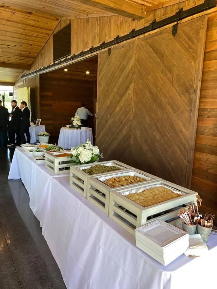 Buffet table with various dishes, napkins, and utensils at a rustic indoor event with wooden walls and a sliding barn door.