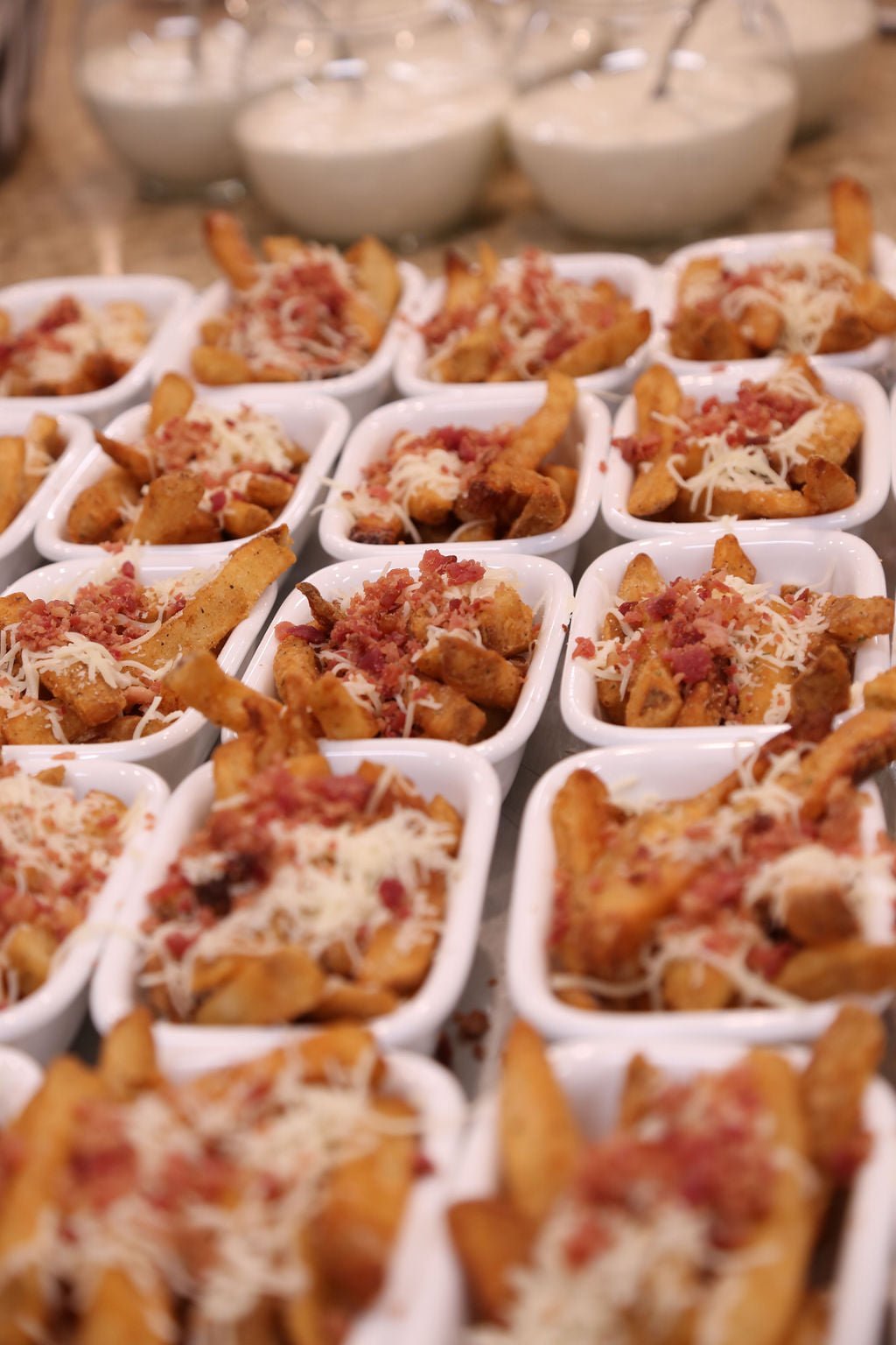 Multiple small white bowls of loaded potato wedges topped with shredded cheese and bacon bits.