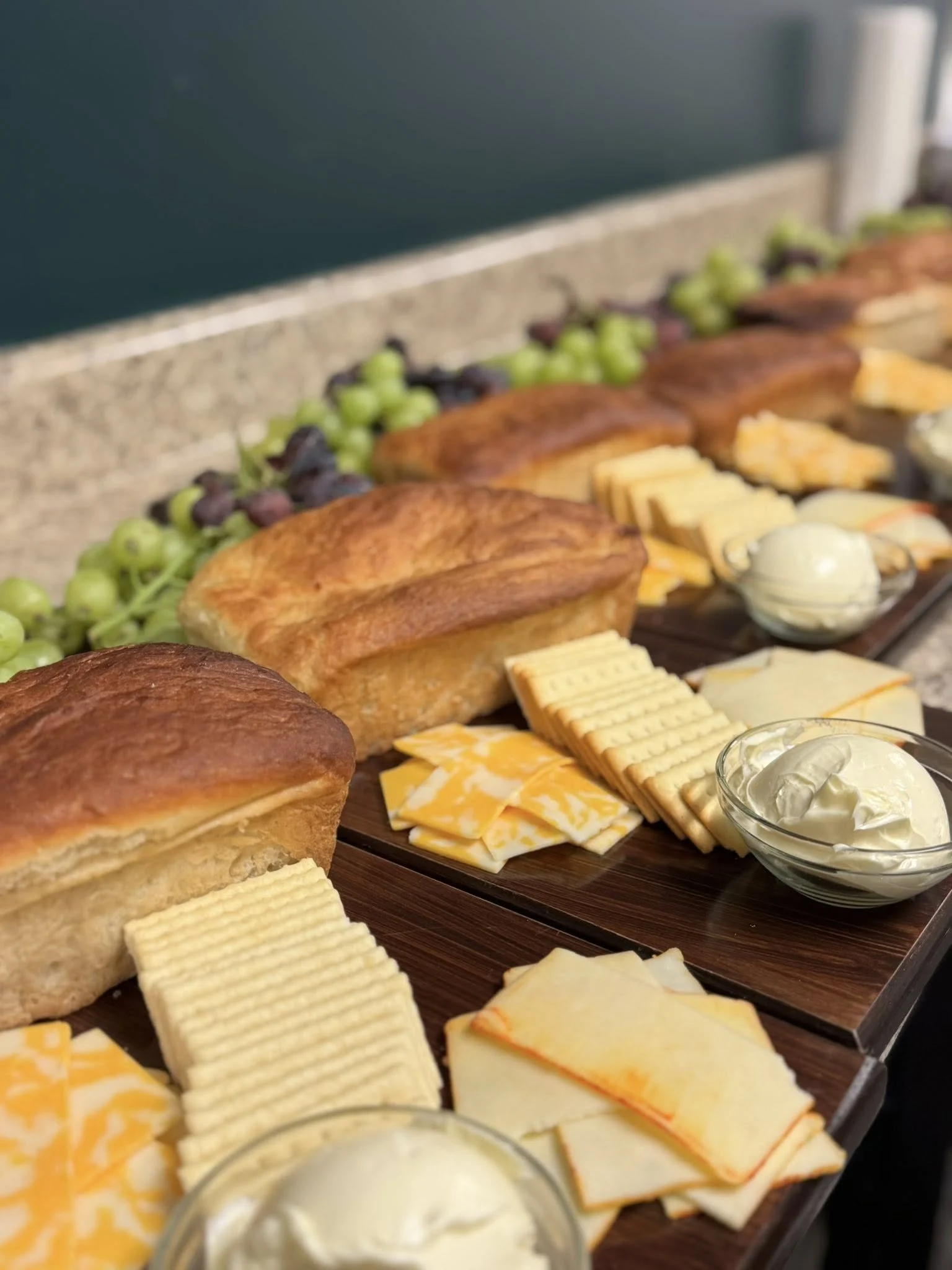A breakfast tray with pastries, cheese slices, crackers, grapes, and bowls of cream cheese.