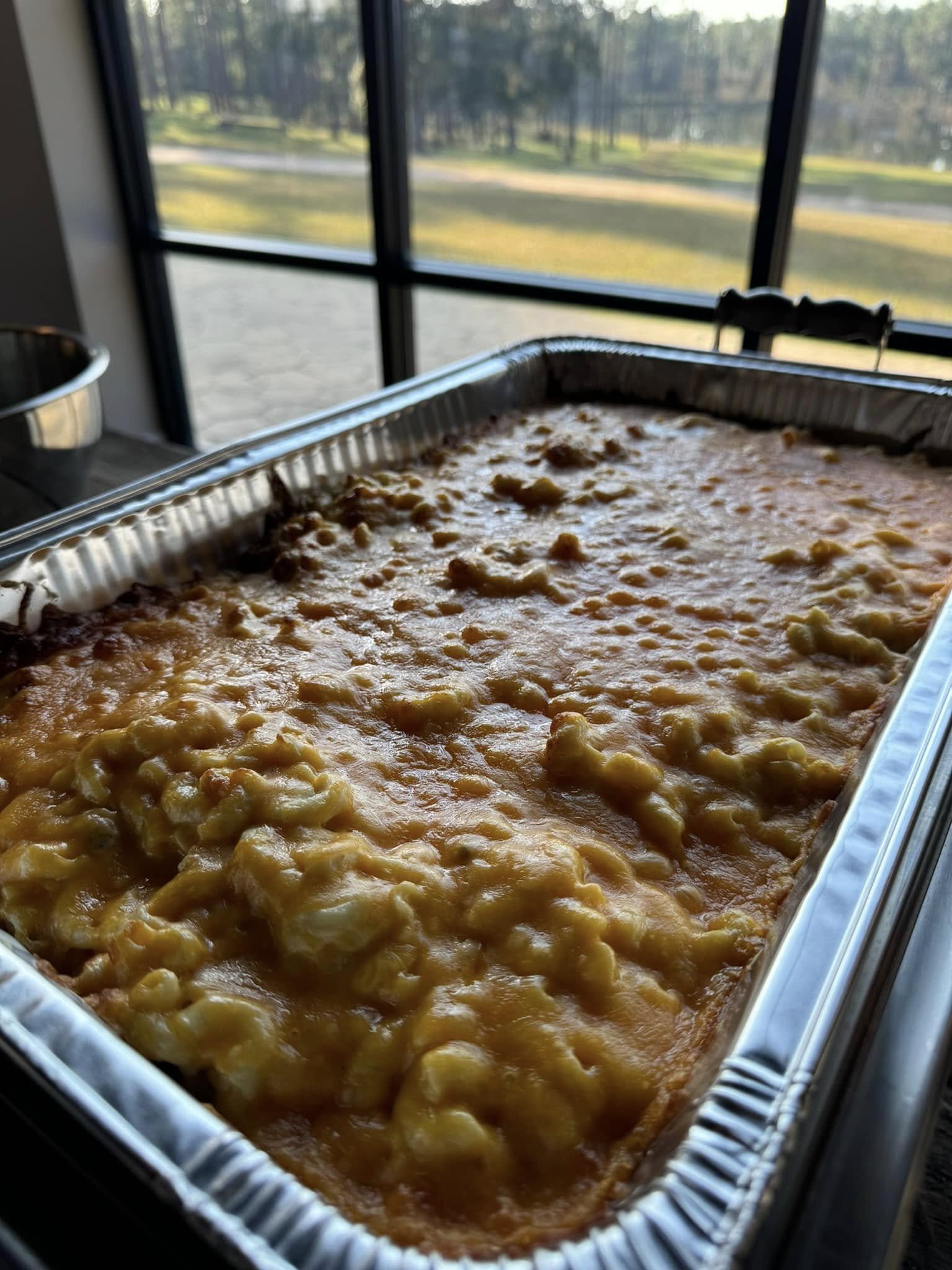Cheese lasagna in a large aluminum tray in front of a window with a scenic outdoor view.