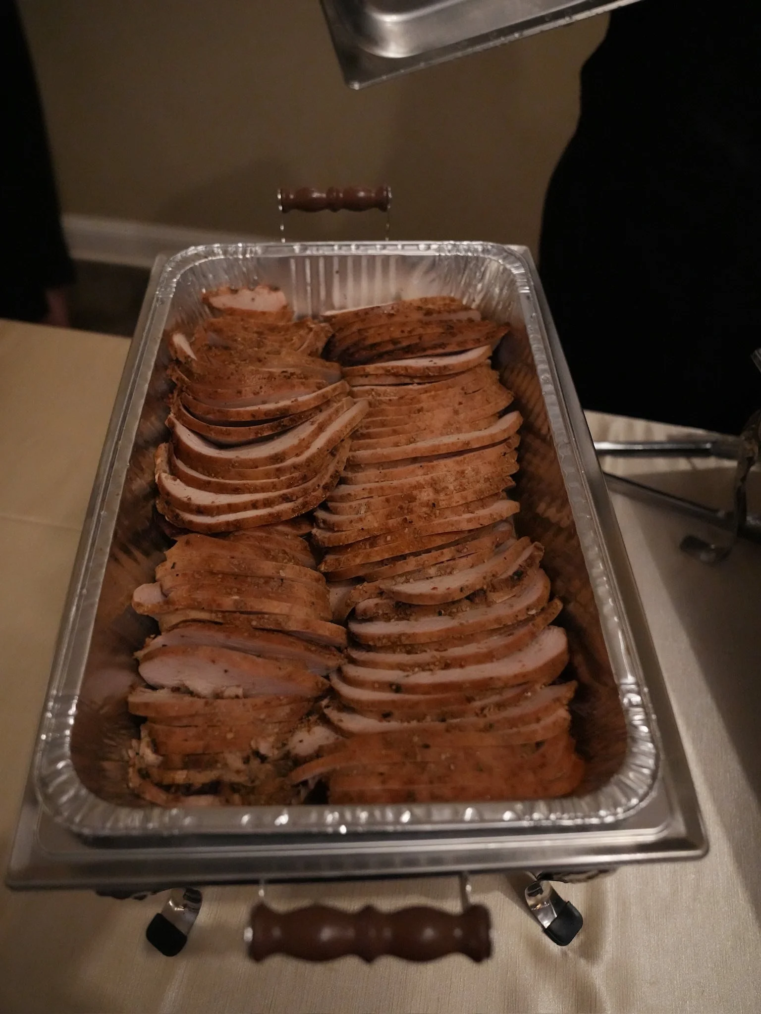 Sliced cooked turkey breast in a large aluminum tray with a carved end piece visible.
