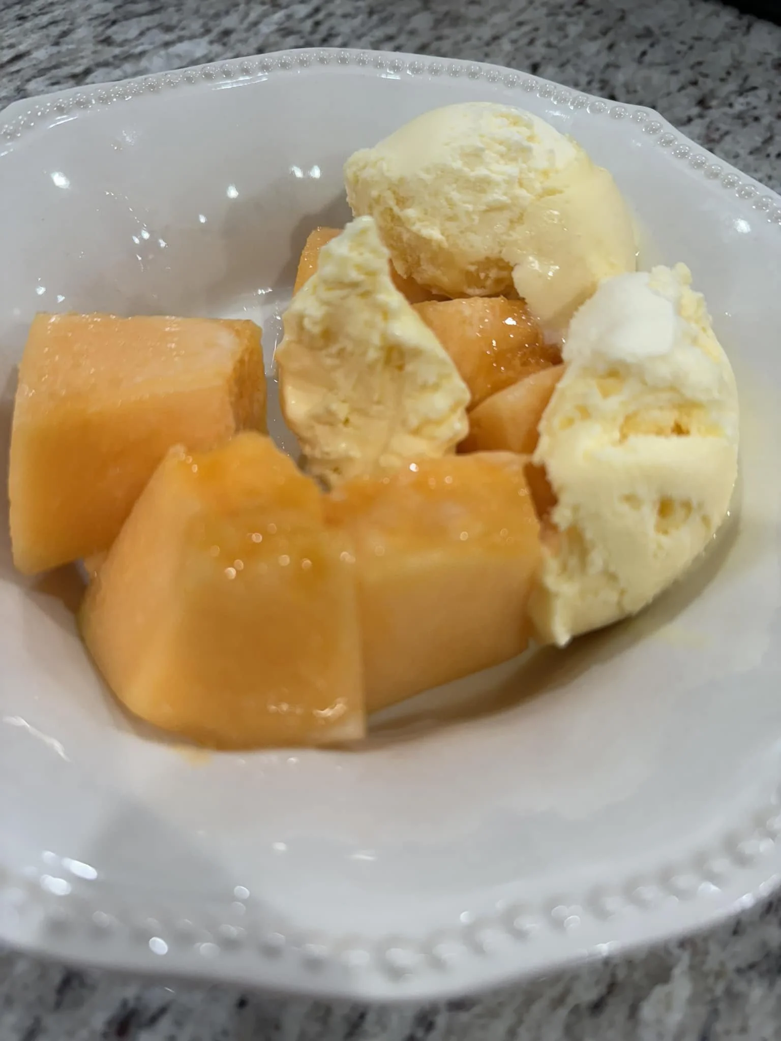 A bowl of vanilla ice cream with chunks of cantaloupe melon on a table.