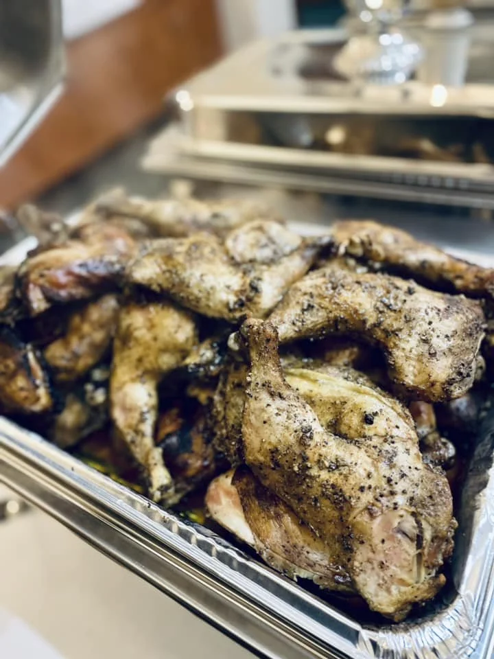 An aluminum tray filled with cooked, seasoned chicken pieces, likely prepared for serving.
