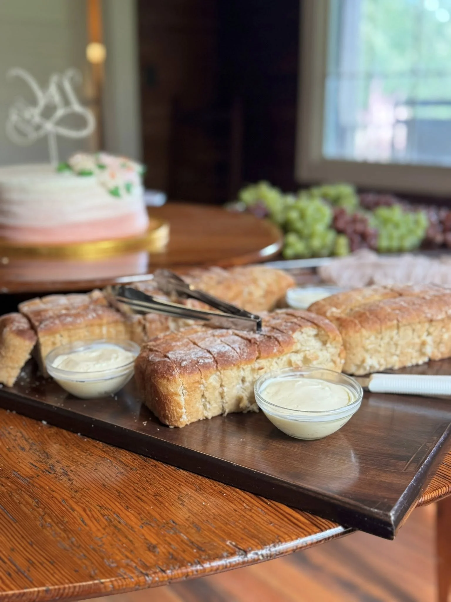Slices of bread with cream, on a wooden tray with a cake in the background.