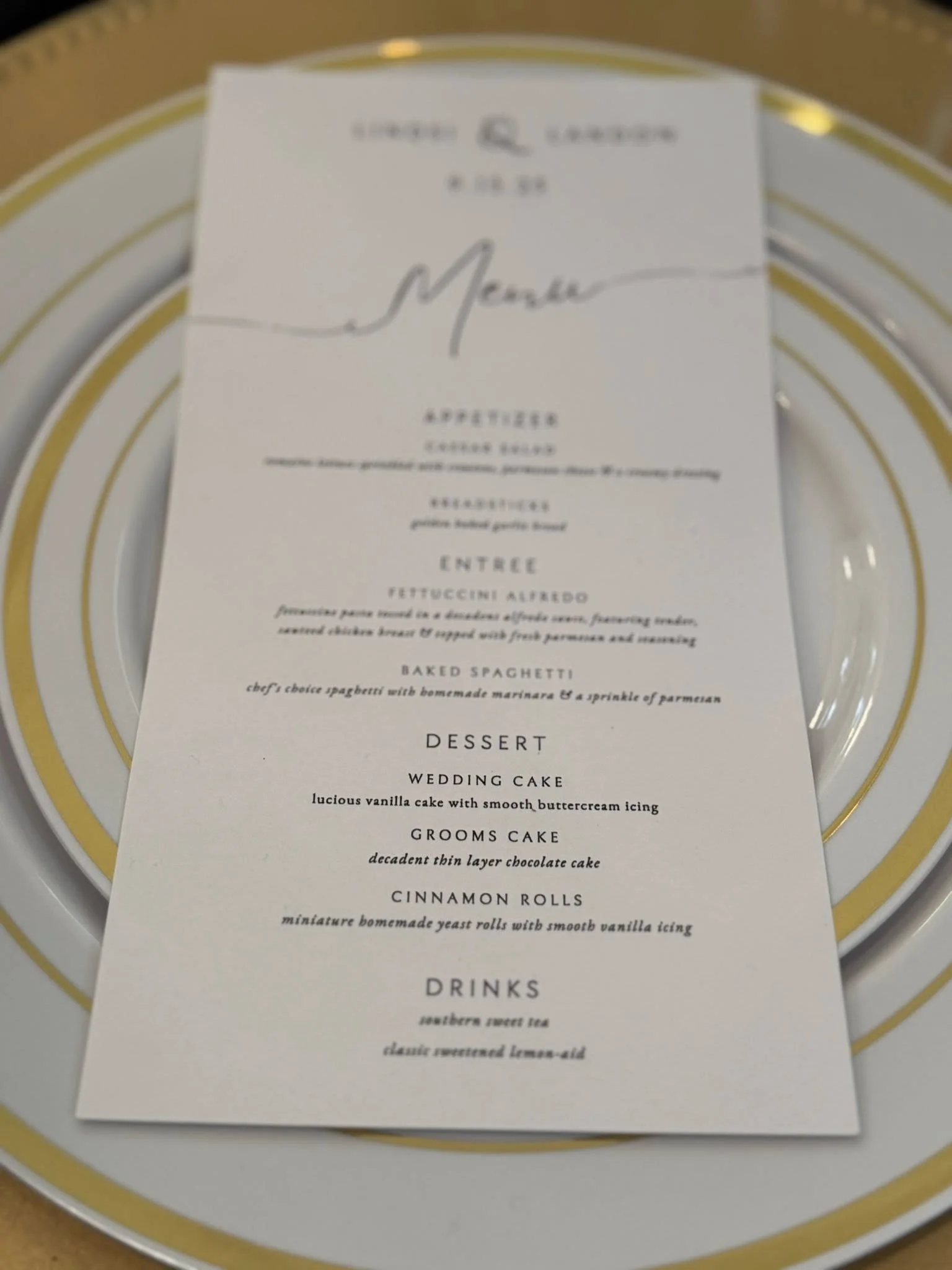 Elegant wedding menu on a white card with black and cursive text, placed on a gold and white striped plate.