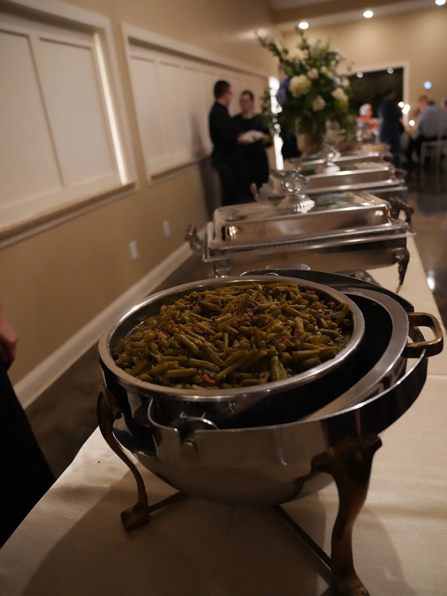 Chafing dish filled with green beans at a buffet table at a social gathering or event.