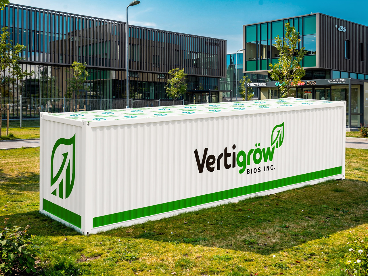 White shipping container with green and black logo and text reading 'Vertigrow BIOS INC,'. The container is outdoors on grass with modern office buildings and trees in the background.