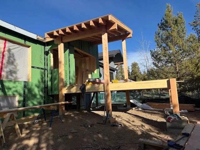 Construction site of a wooden deck attached to a house, with framing in progress and construction tools nearby.