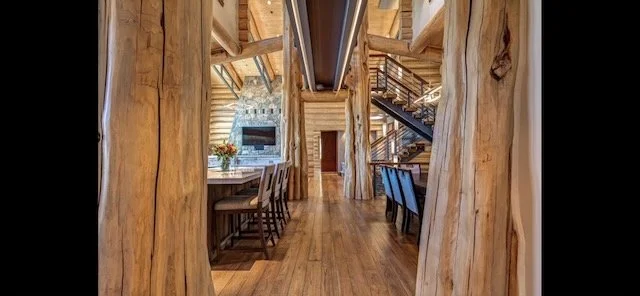 Interior of a log cabin with wooden beams, staircase, and seating area.
