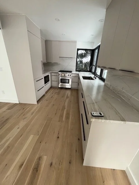 Modern kitchen with white cabinets, a stainless steel stove, and a large window with a view of trees.