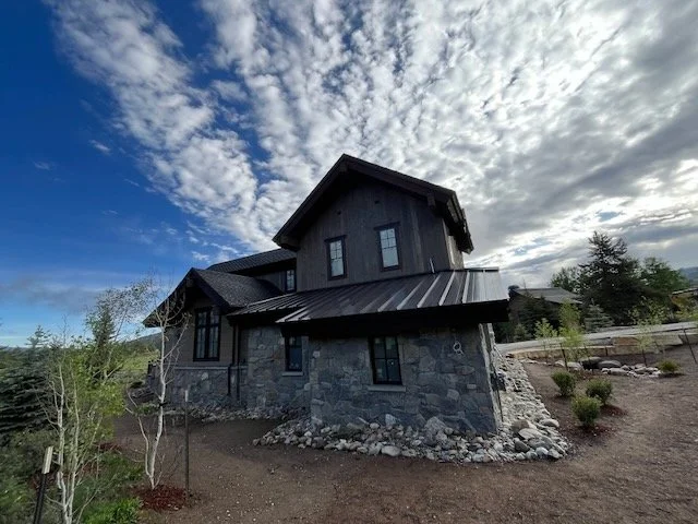 A black house with stone exterior walls and a metal roof, set against a cloudy sky. Breckenridge Colorado Construction