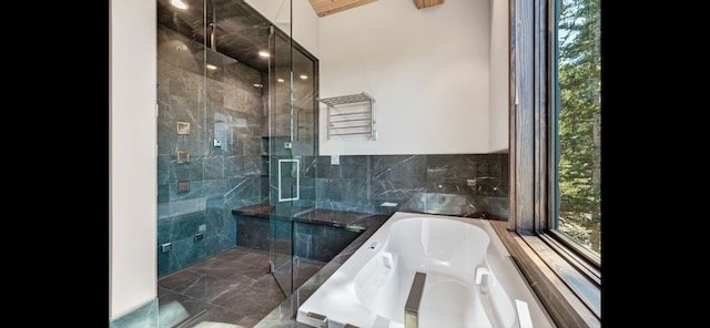 Modern bathroom with a glass-enclosed shower, a corner bathtub next to large windows, and a wooden ceiling beam.
