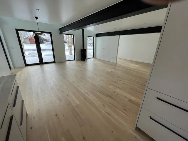 Empty room with large windows and sliding glass doors, light hardwood floors, modern white cabinetry, and a ceiling-mounted light fixture.