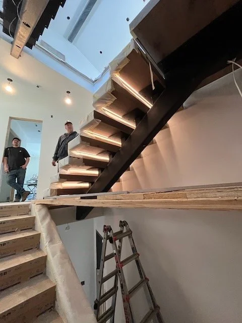 Interior view of a staircase under construction in a modern home, with two workers present and construction tools nearby.