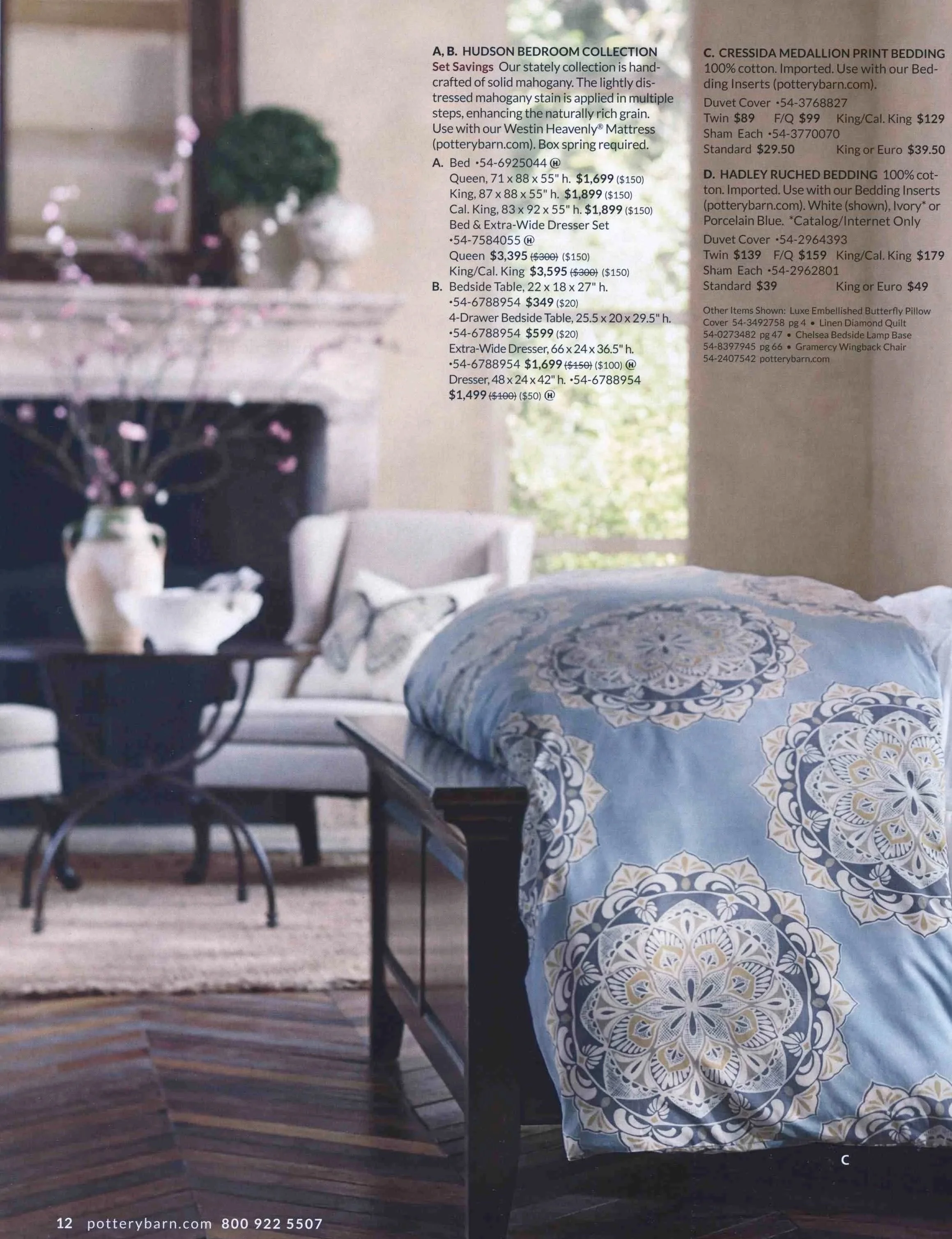 Interior Styling  of a bed with a blue and white ornate patterned bedspread, on a wooden deck, with a table and chairs in the background and a vase of small pink flowers in the foreground.