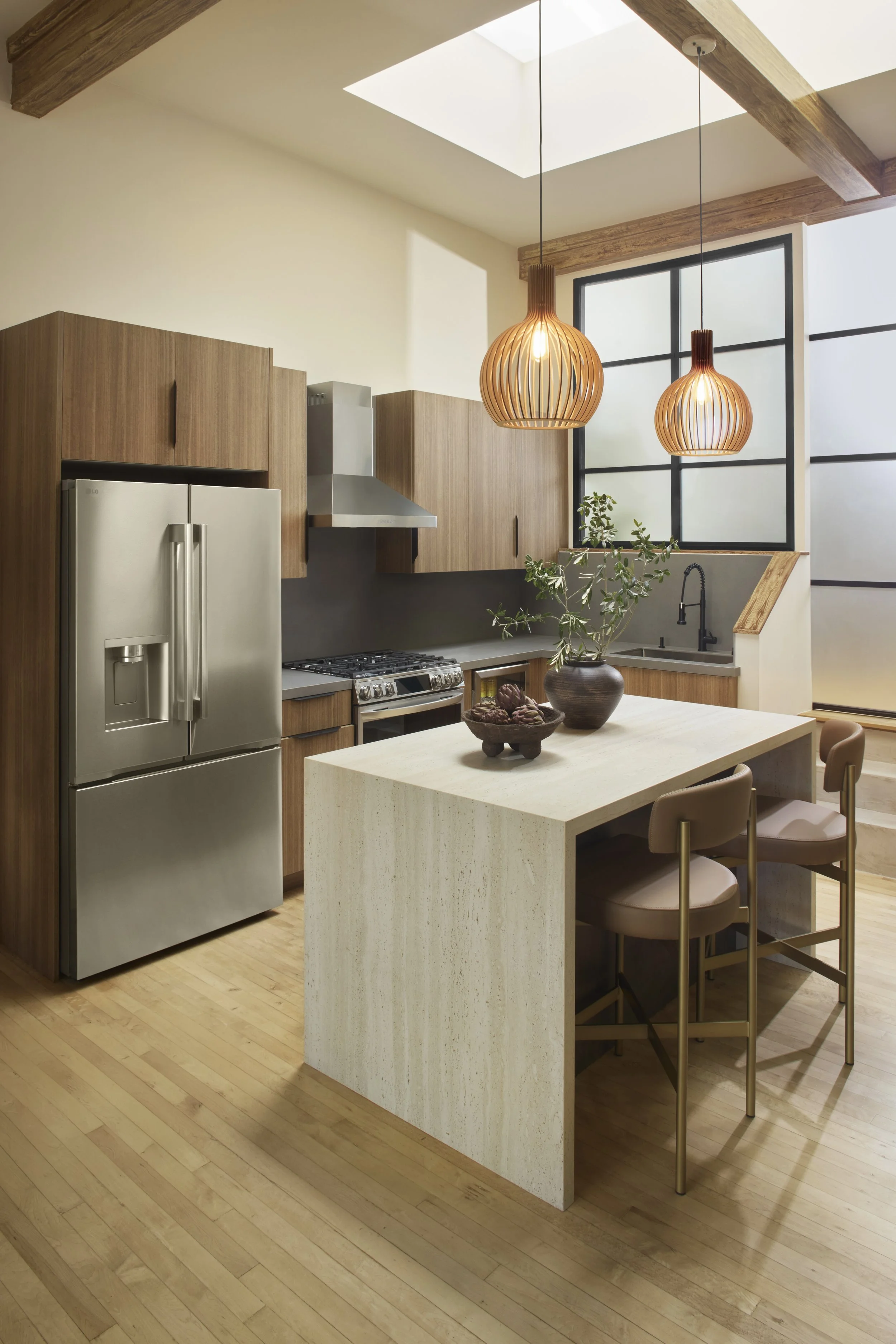 Modern kitchen with wooden cabinetry, a stainless steel refrigerator, a stove, and a sink. Two hanging pendant lights with wooden slats, a plant on the counter, and hardwood floors.