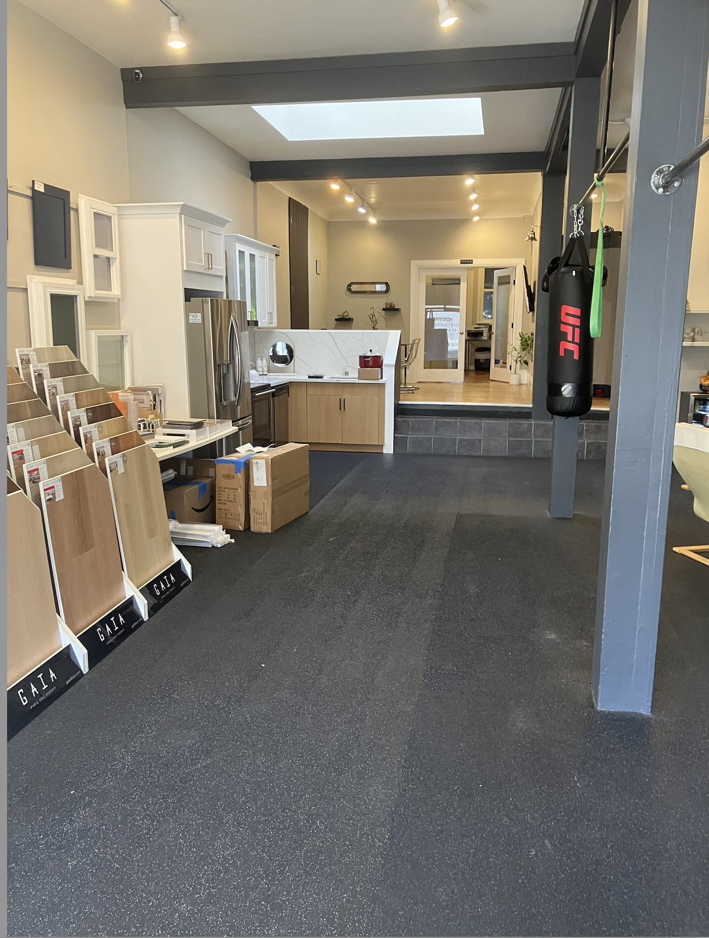 Front of Showroom; old black gym mat floors, black painted beams with track lighting and in need of a  lot of work.