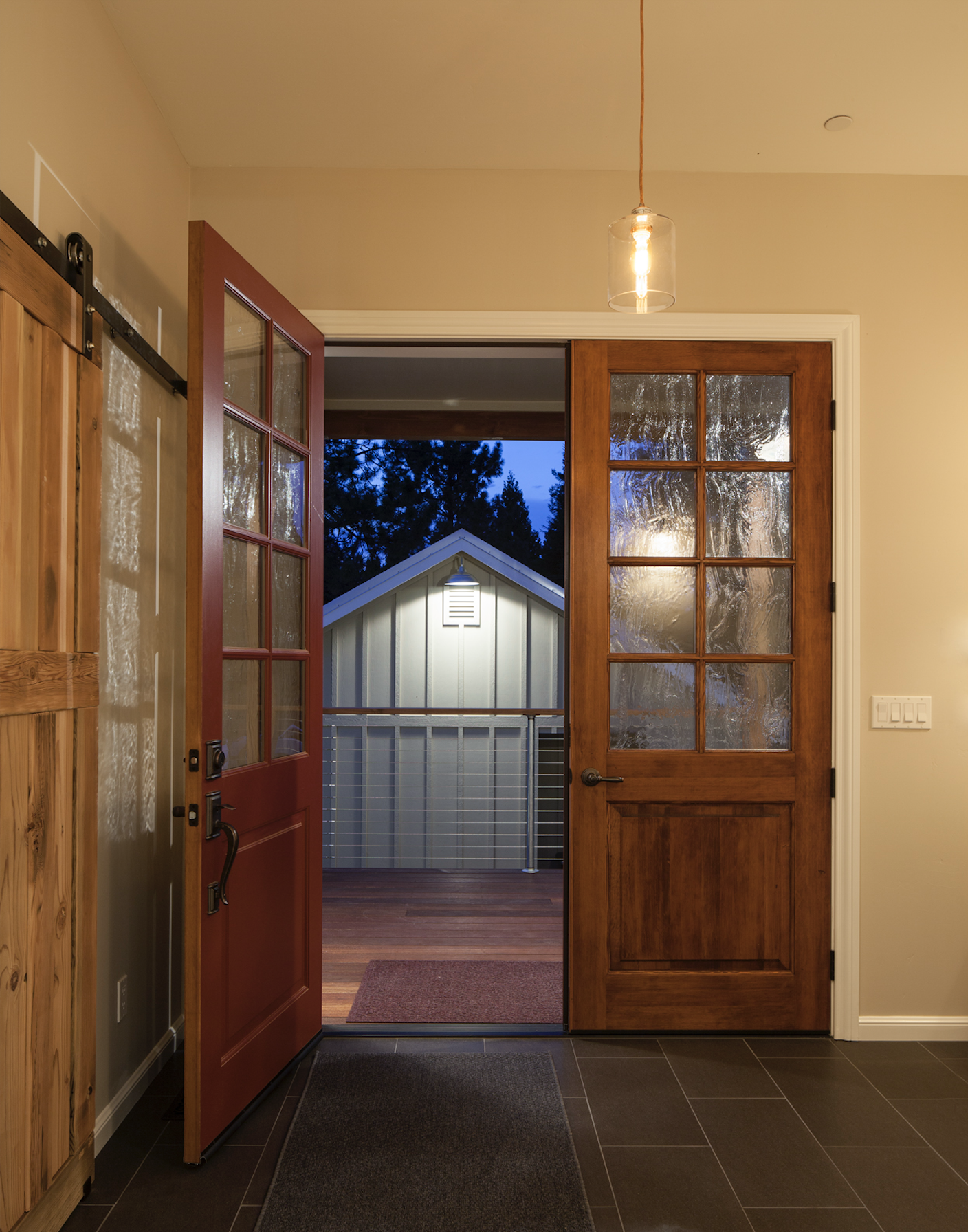 Open door leading from an indoor space to a porch at dusk, with trees and a small building visible outside, with warm interior lighting.