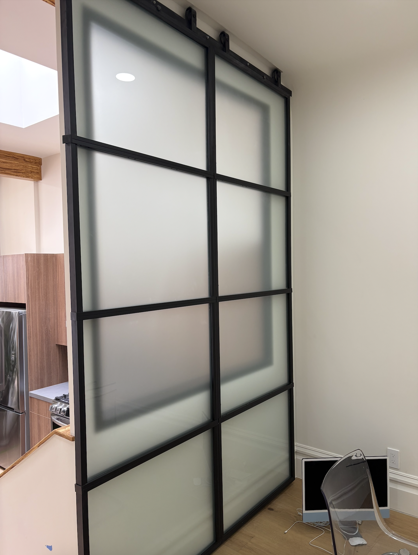 Frosted glass sliding door with black metal frame separating a kitchen from an office or living space.