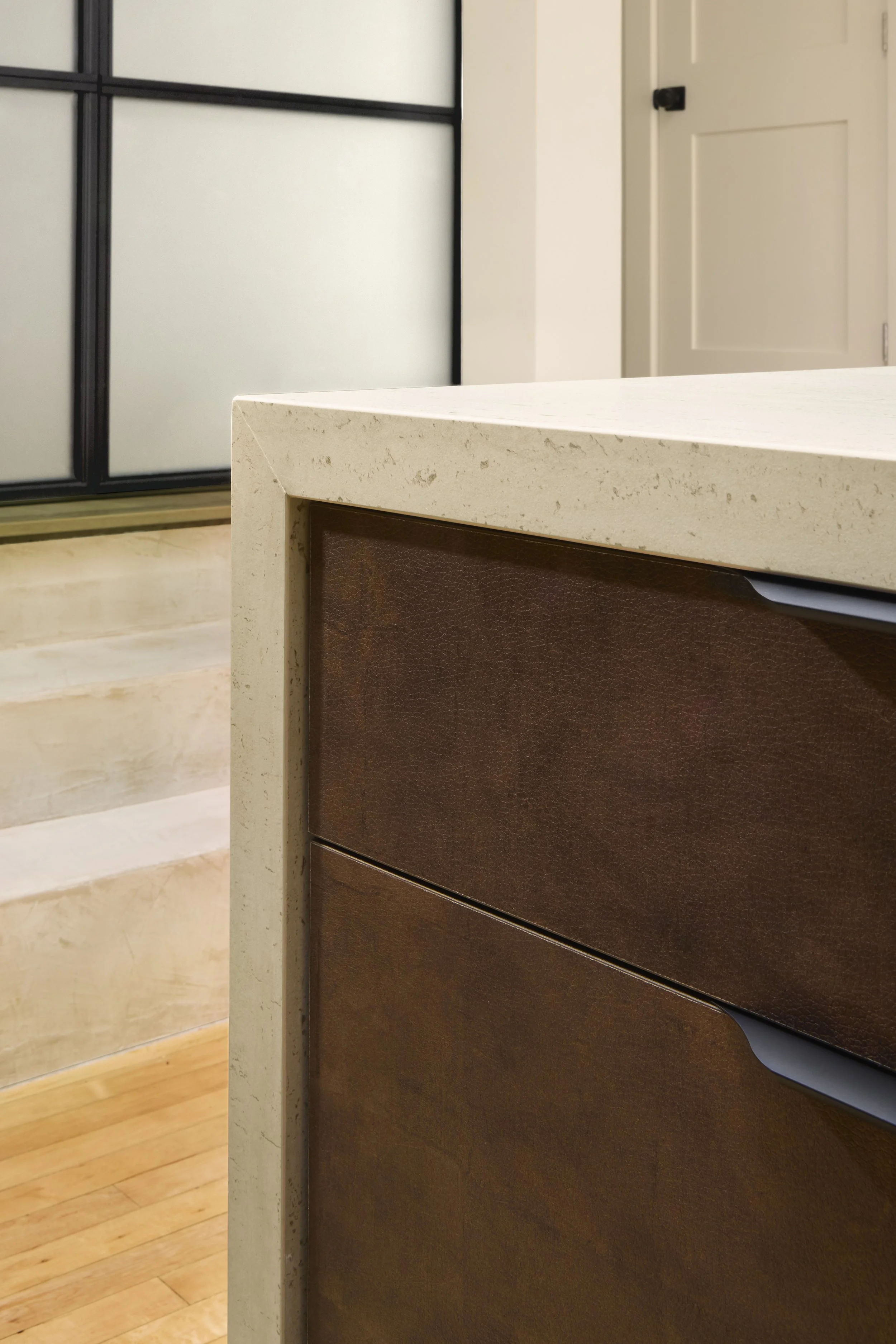 A close-up view of a beige kitchen countertop with a brown cabinet underneath, with a background showing a sliding door with frosted glass panels and a white door in a home interior.