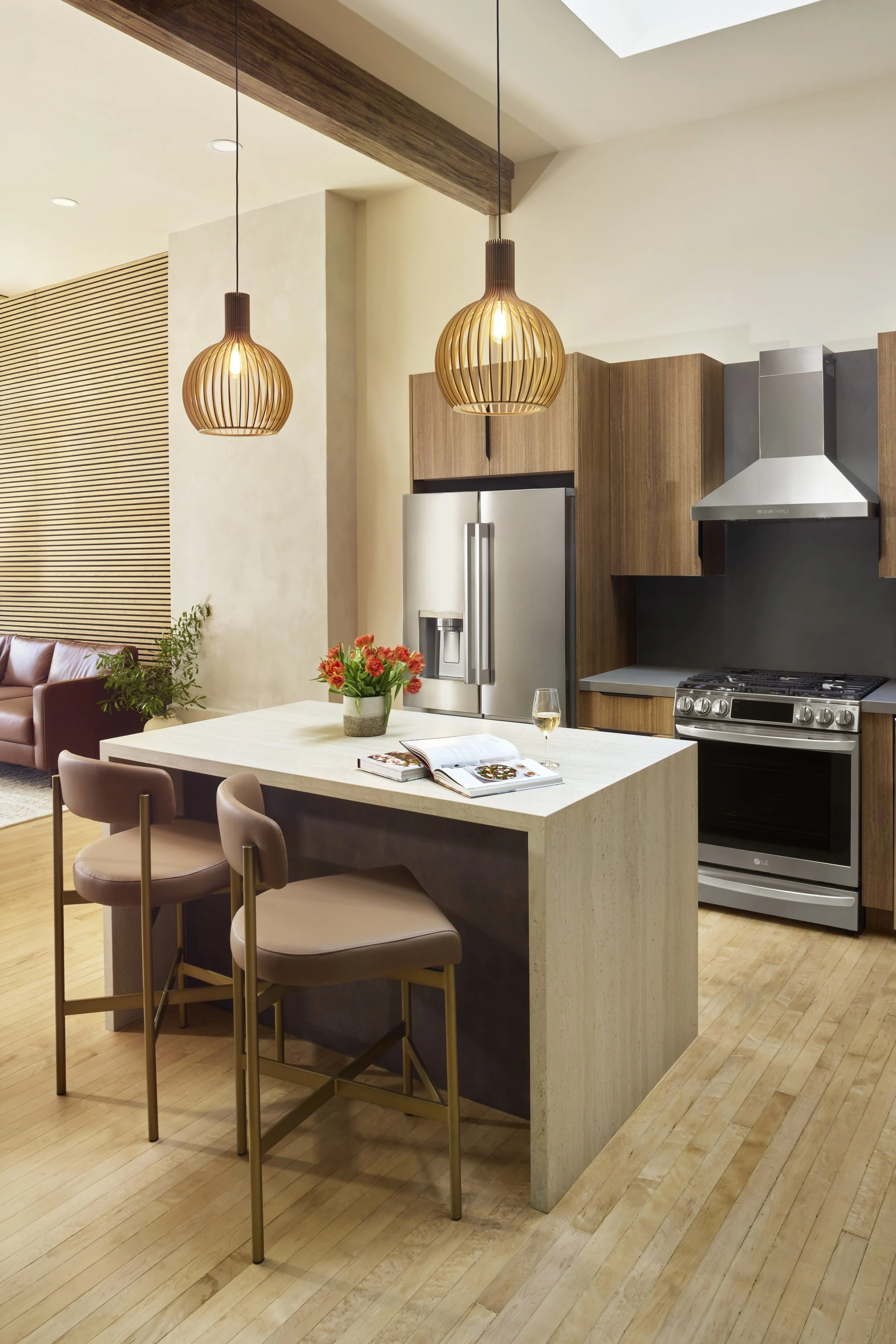 Modern kitchen with pendant lights, a white island table with a flower arrangement, and adjacent seating area with beige chairs and a mauve sofa.
