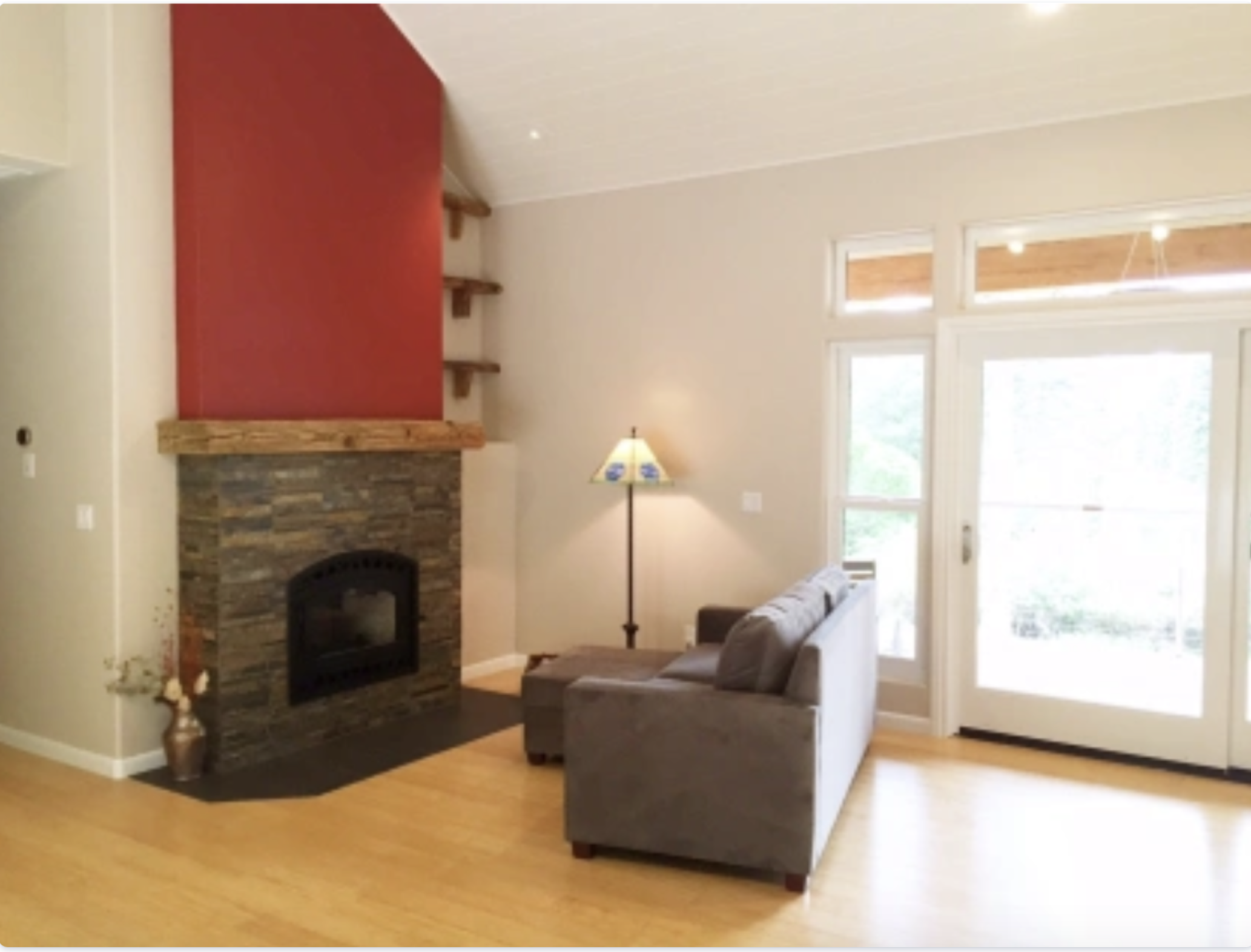 Living room with a fireplace, beige walls, large windows, sofa, floor lamp, and hardwood flooring.