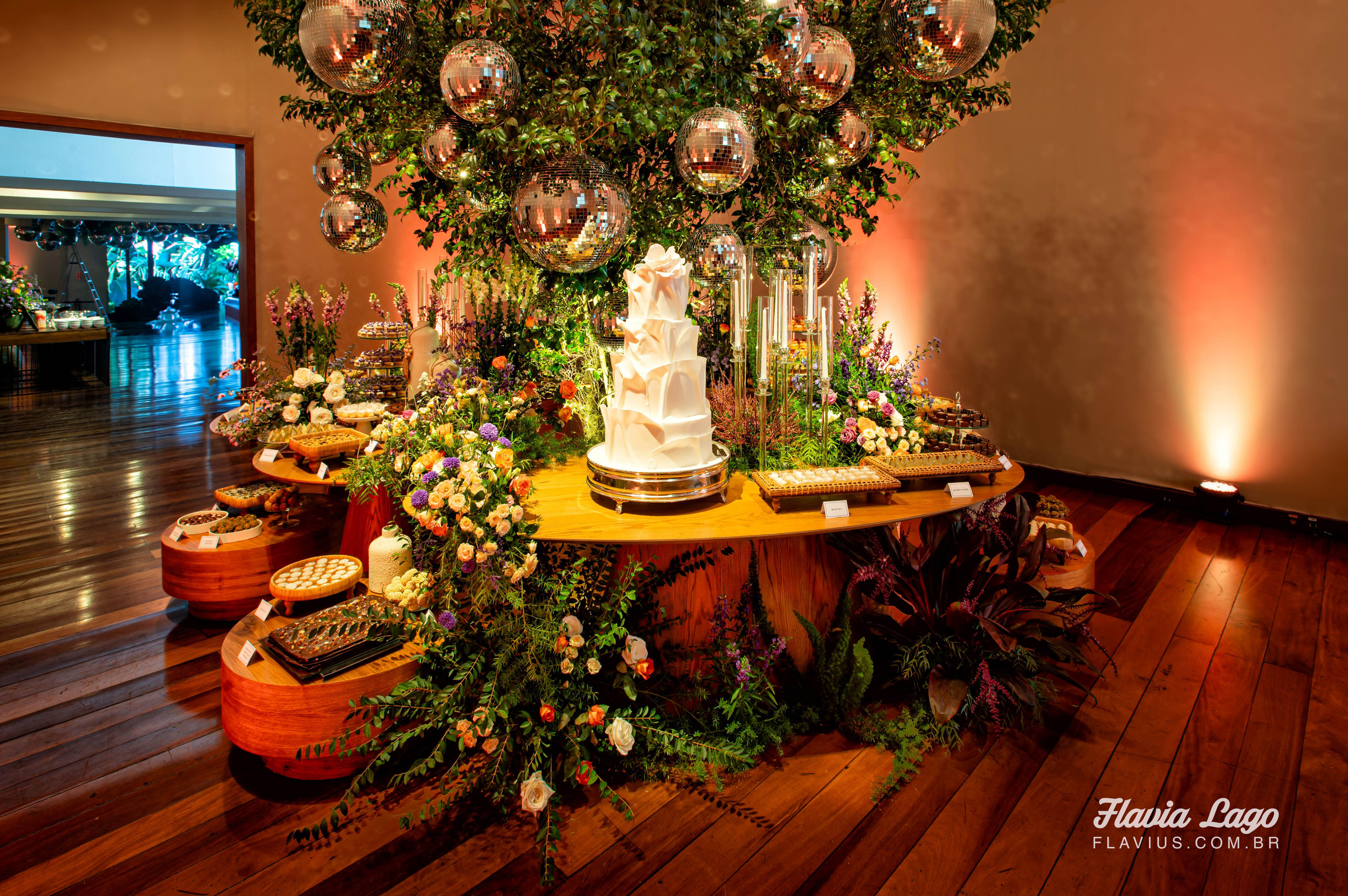 mesa de bolo e doces central na spazio itanhangá com arvore de folhas e globos de espelho