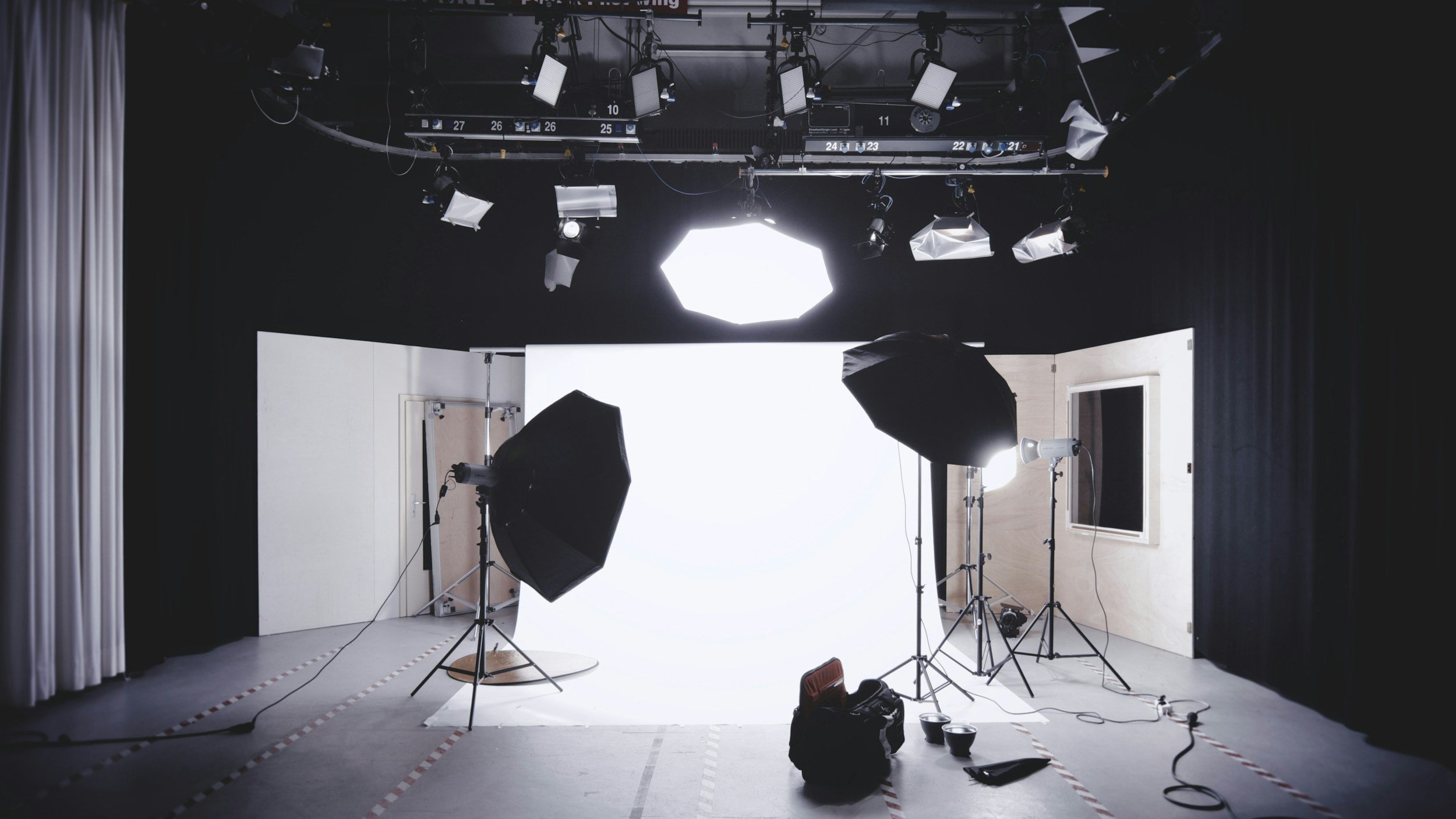 A professional photography or video studio with lighting equipment, softboxes, and a white backdrop, set up for a shoot.