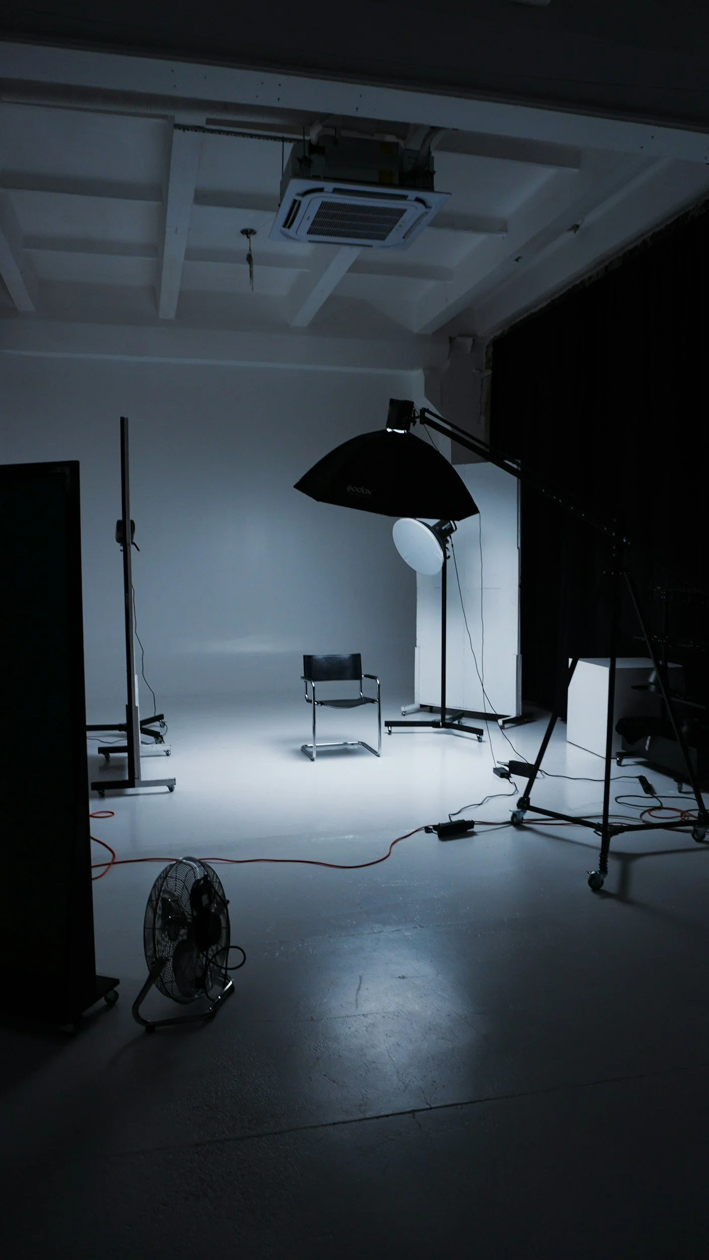 Photography studio with white background, black chair, studio lights, softbox, and a fan on the floor.