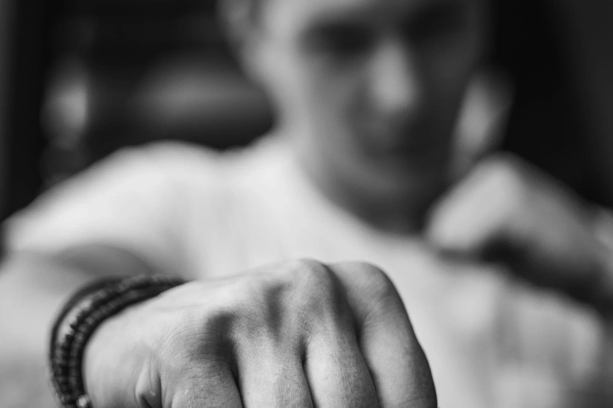 Close-up black-and-white photo of a person's fist with a ring on their finger, taken from below, with the background out of focus.