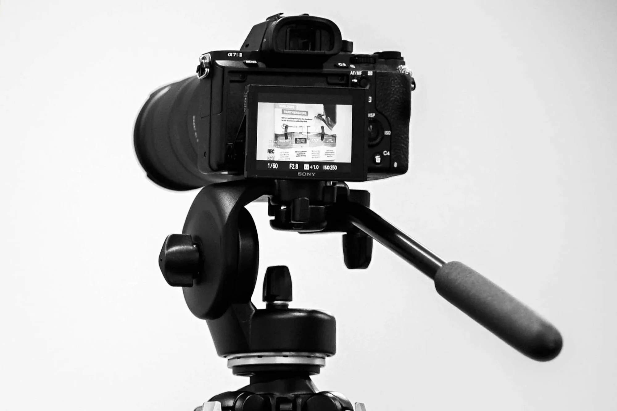 Black digital camera on a tripod against a plain white background.