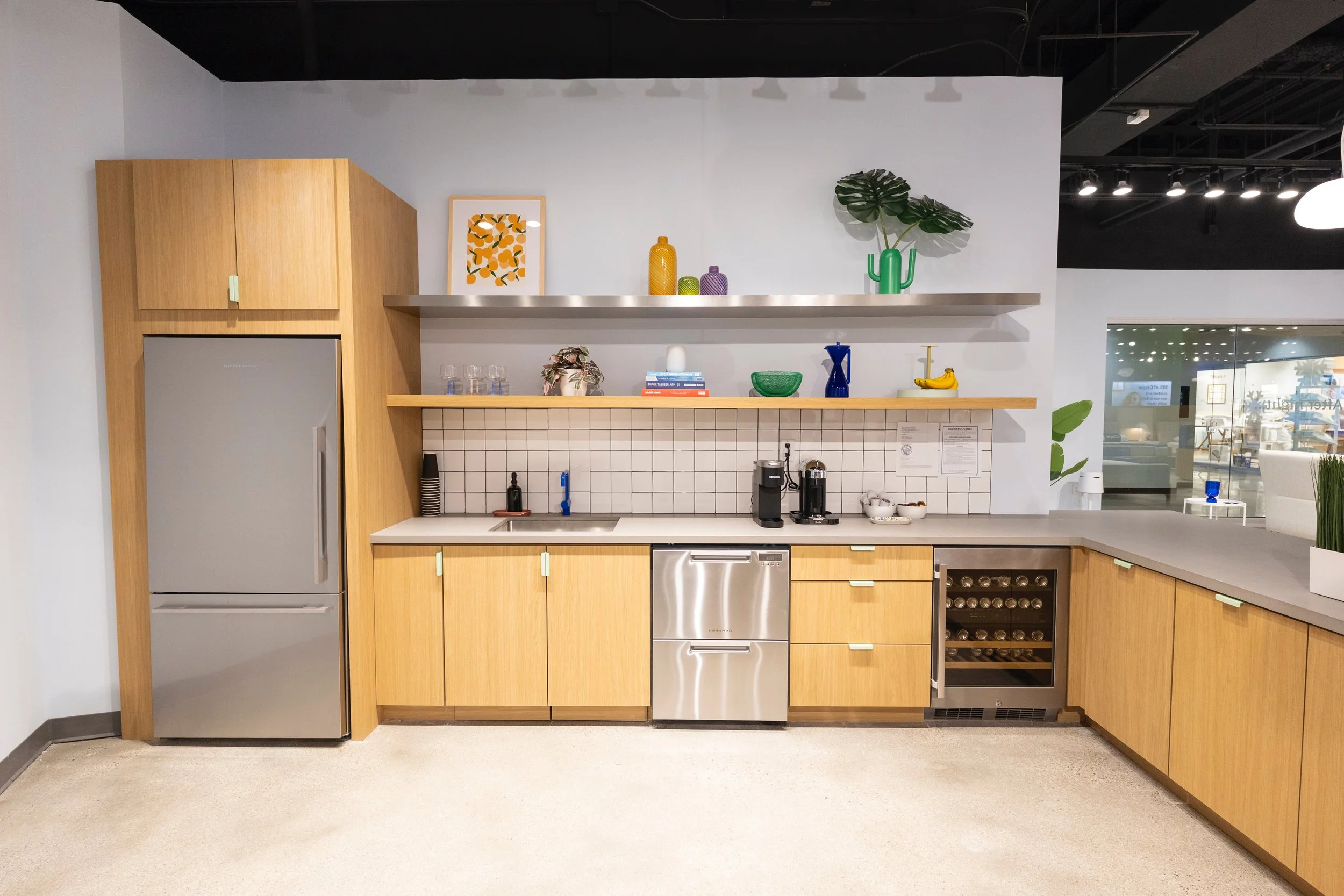 Modern kitchen with wooden cabinets, stainless steel appliances, and open shelving decorated with colorful vases, artwork, plants, and kitchenware.