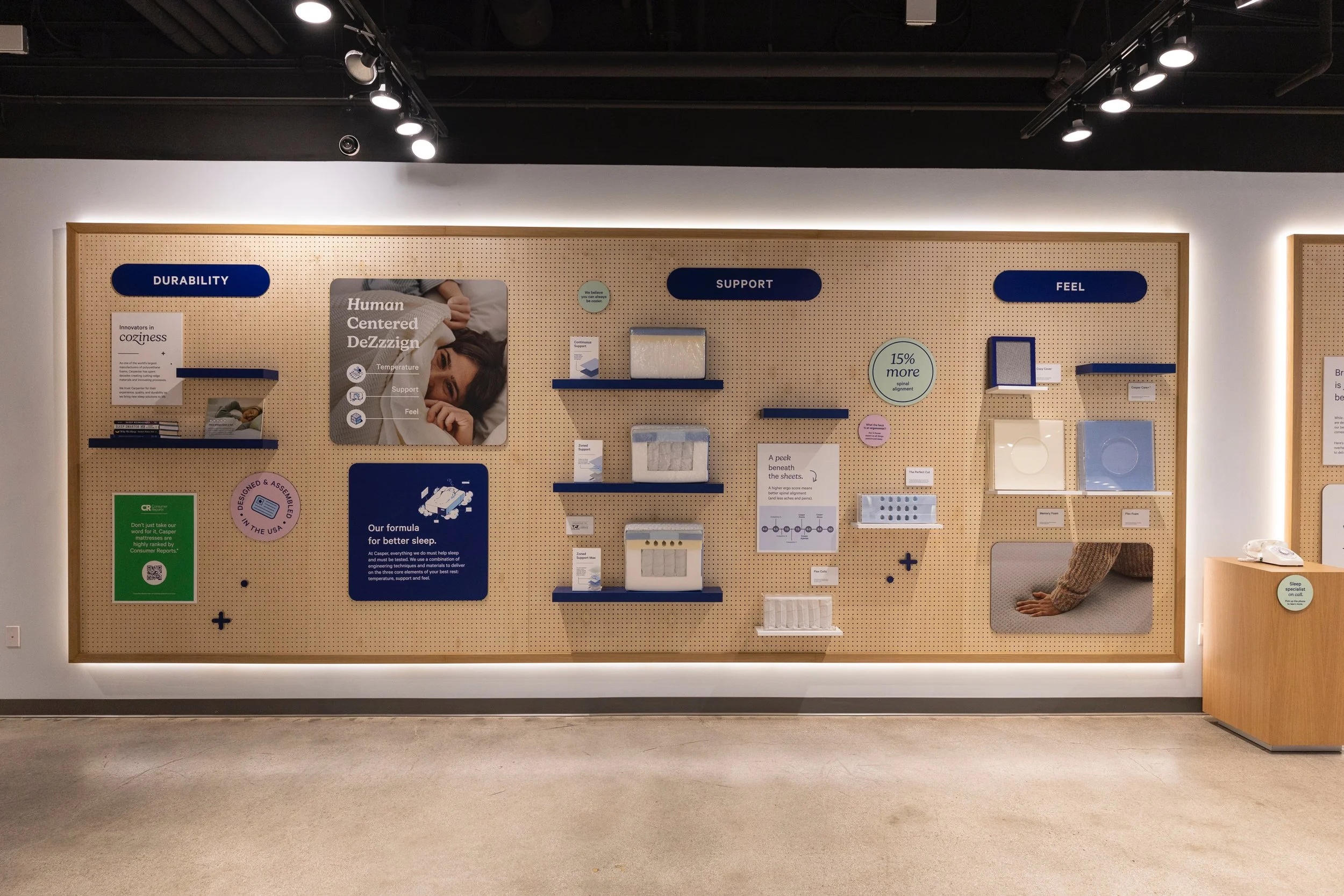 A display wall with informational posters and samples about human-centered design and sleep products, featuring blue and white color themes, under spotlights in a modern retail or exhibit space.