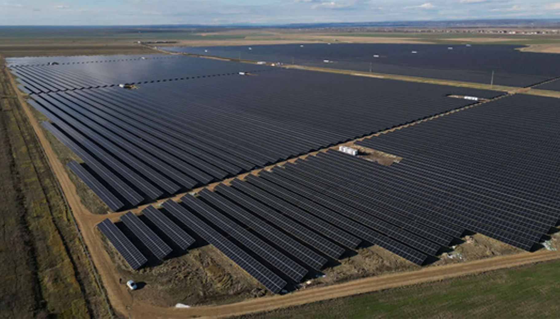 A large solar farm with rows of solar panels on a flat, open landscape during daytime.
