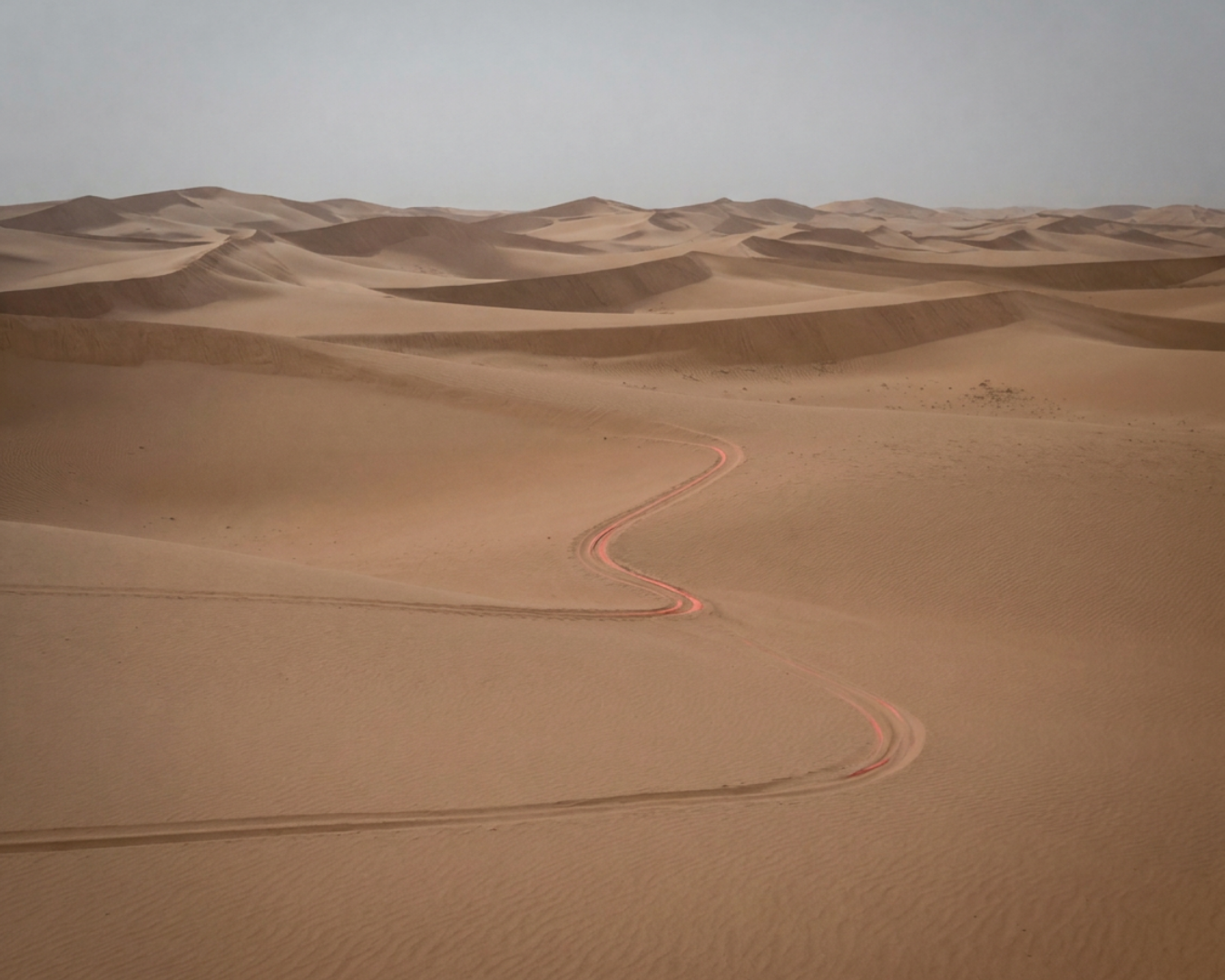 A cinematic view of vast, rolling desert sand dunes under moody, analytical lighting, featuring a single, winding track with a glowing red outline symbolizing a biomechanical mechanical leak.