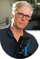 A middle-aged man with gray hair and glasses standing next to a scientific or laboratory instrument.