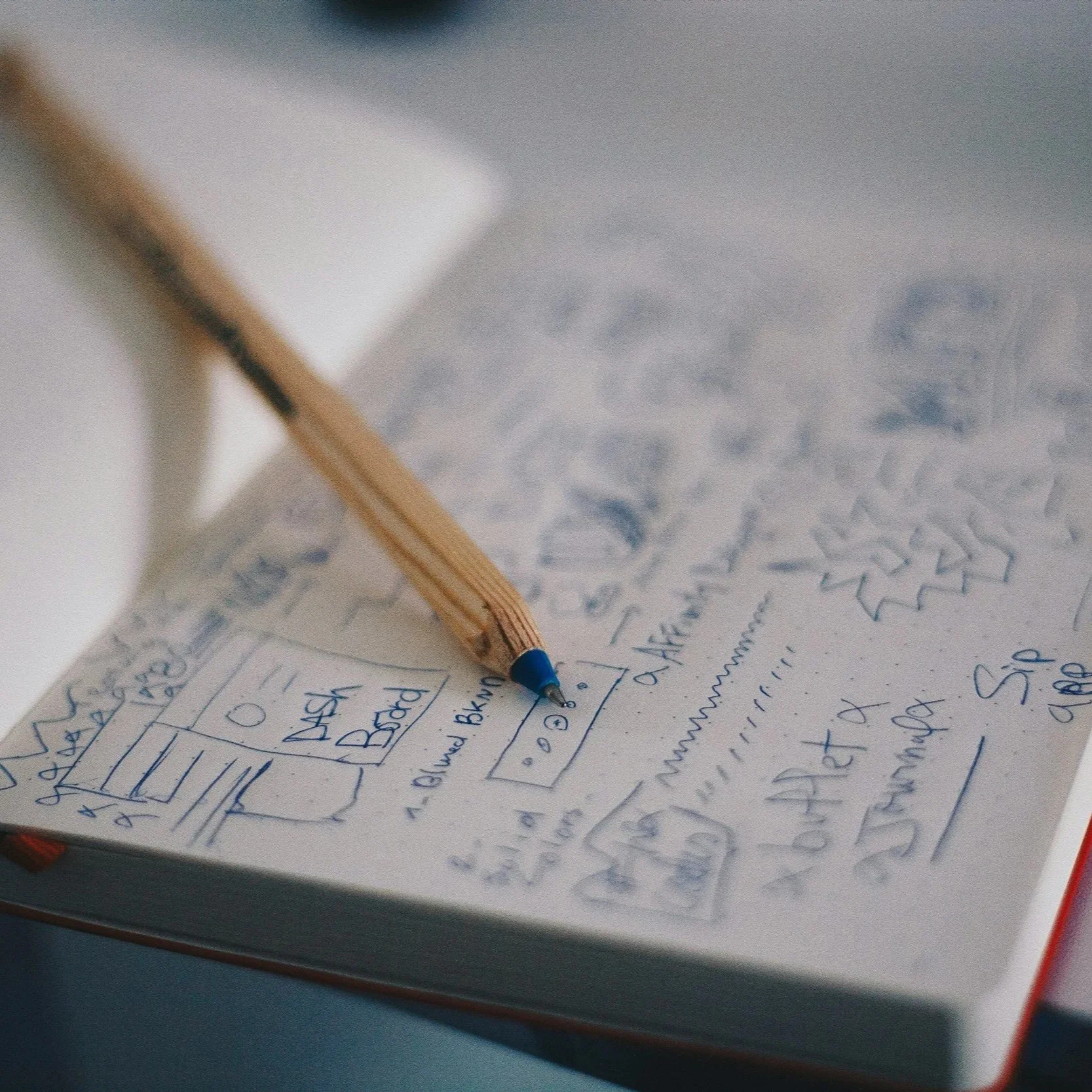Handwritten notes and sketches on a notepad with a wooden pencil resting on the paper.