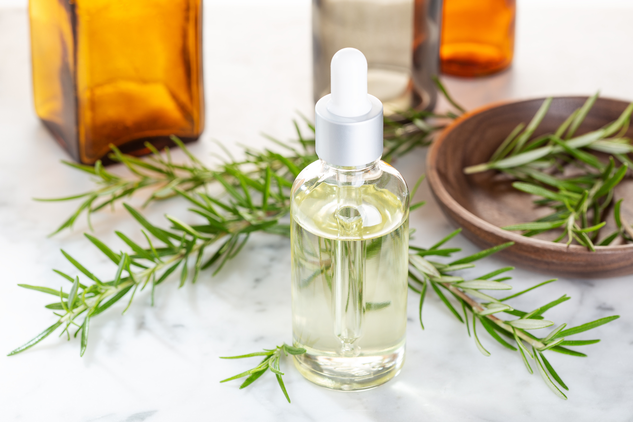 Small dropper bottle of botanical pesticide minimum risk liquid formula surrounded by fresh rosemary and natural plant extracts, representing Bug Brothers LLC's EPA/FIFRA 25(b) exempt ingredients.