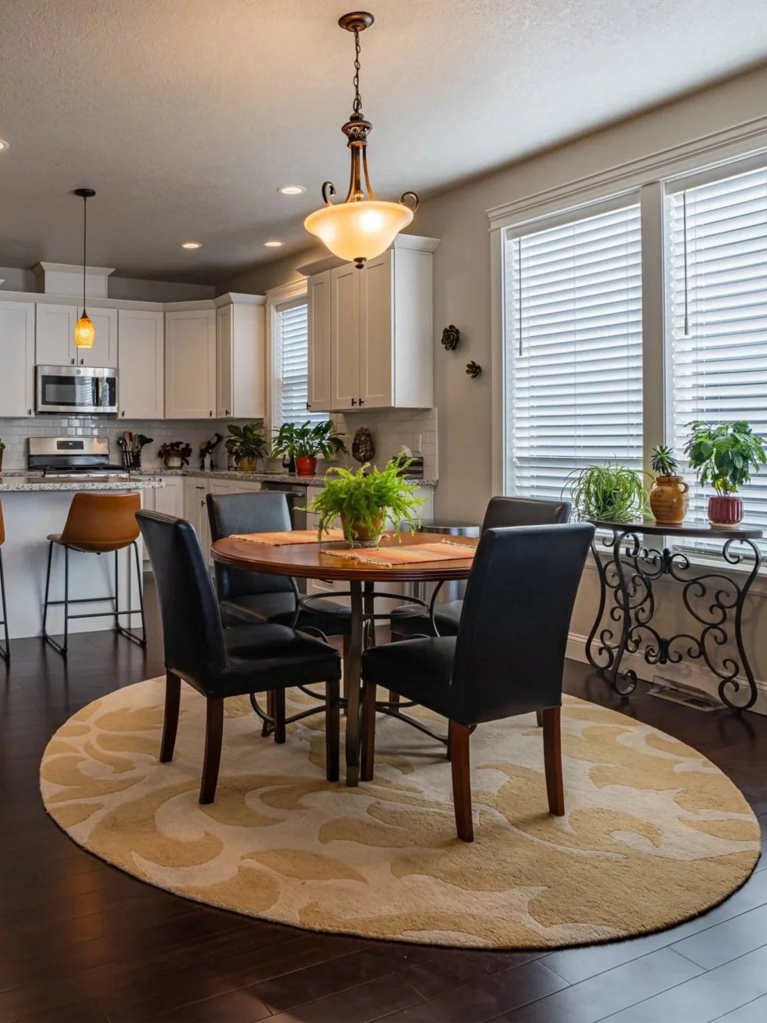 Open-plan dining room and kitchen in a Salem, Oregon home featuring dark hardwood floors, round dining table, pendant lighting, white shaker cabinets, and stainless steel appliances