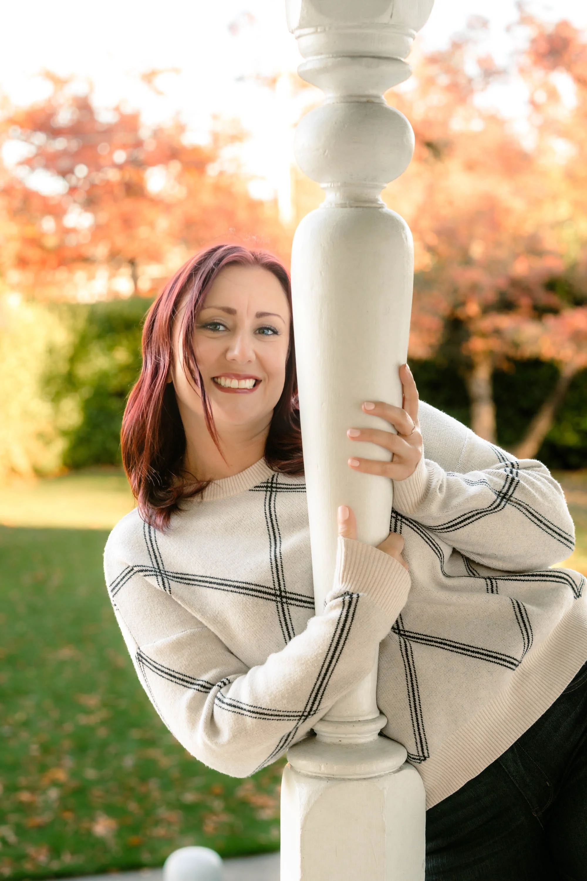 Havenrose Real Estate broker and relocation specialist Katy Voves smiling beside a white porch column with fall foliage in Salem, Oregon