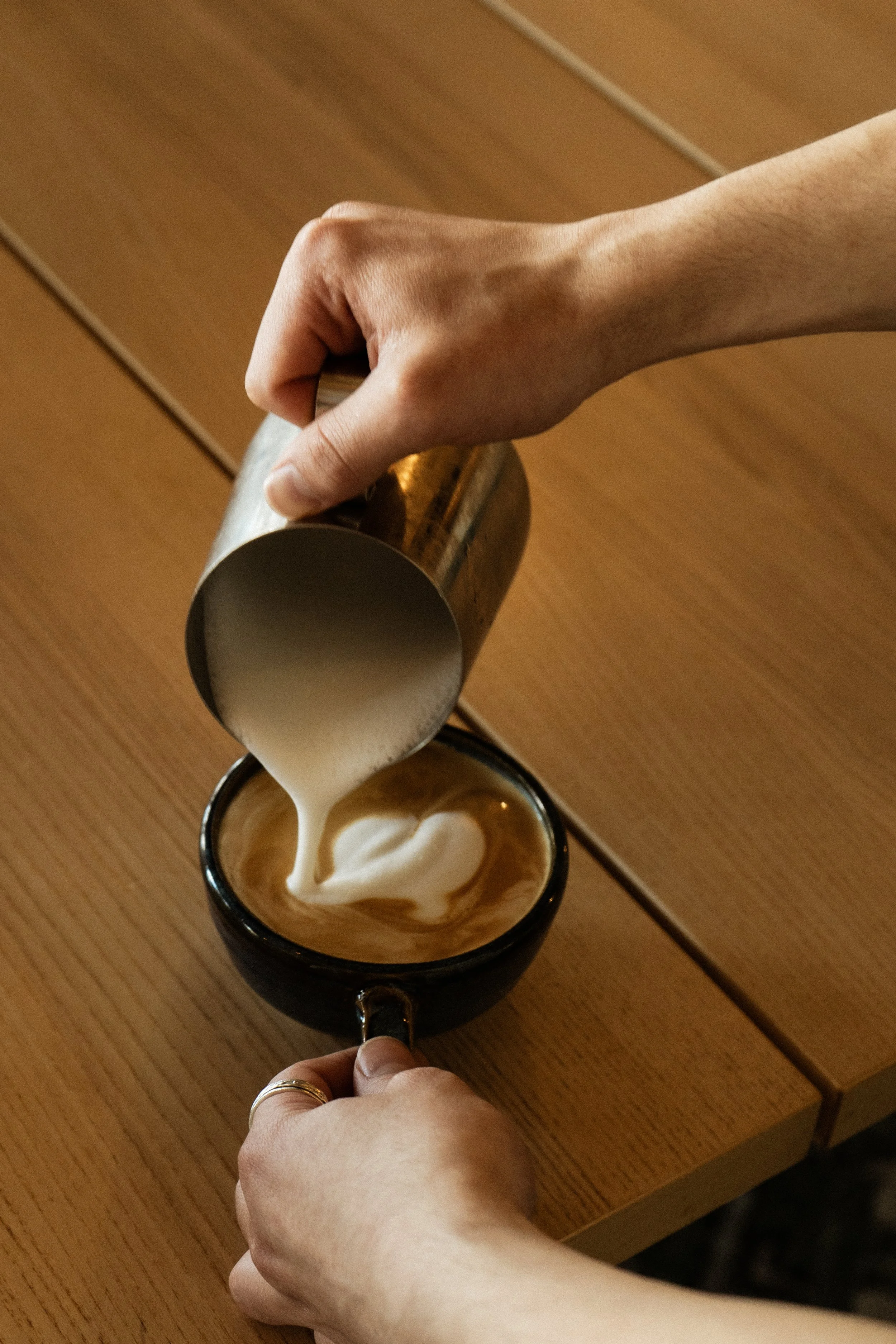 A person is pouring steamed milk into a cup of coffee, creating latte art on the surface.