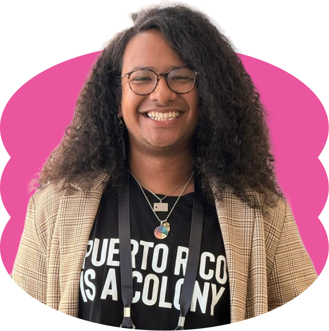 Joniel R. Pacheco Muñoz is smiling, with long curly hair and glasses, wearing a black shirt and a checkered beige suit jacket, placed over a scalloped hot pink oval shape.