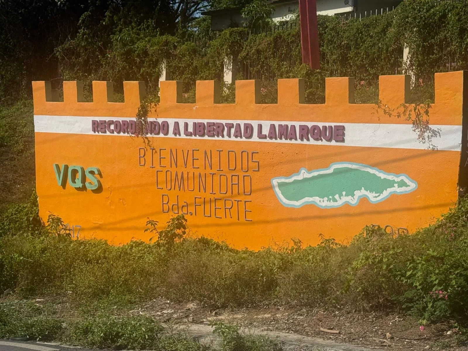 Colorful painted mural on an orange wall with a sketch of a town. The mural contains the words 'Recordando a libertad Lamarque,’ and ‘Bienvenidos Comunidad Bda. Fuerte’ in different colors and styles.
