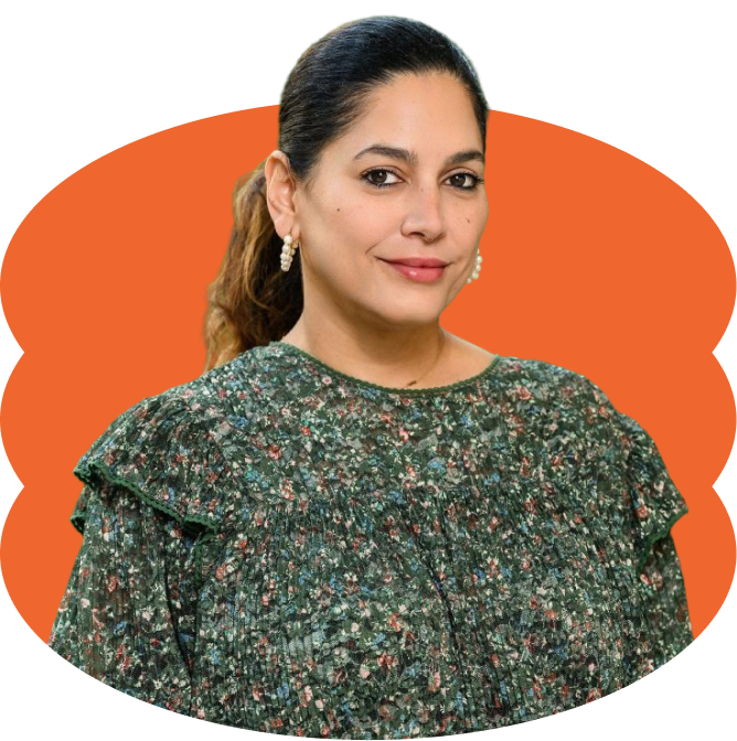 Aurora Santiago Ortiz smiling, with dark hair and blonde highlights tied in a low ponytail, dressed in a dark green floral long-sleeve dress, placed over a scalloped orange oval shape.