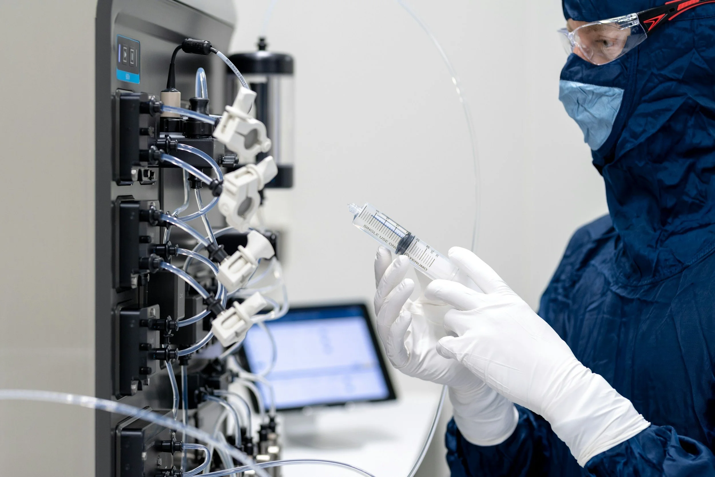 A scientist in safety gear handling a syringe connected to lab equipment in a laboratory.